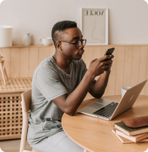 Man checking his phone beside a laptop